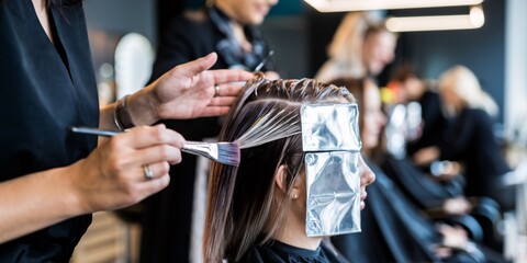 A hairstylist applies color to a client's hair with precision using foil highlights at a modern salon. The foreground focus captures the detailed process, while the background is attractively blurred.