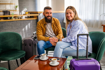Obraz premium Young happy couple is going on vacation. Tourists sitting in hotel lobby and drinking coffee.