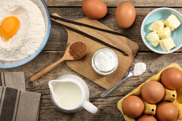Baking powder in bowl surrounded by other products on wooden table, flat lay