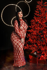 A beautiful young girl plus size model in a red evening dress with bright makeup with a snake. New Year's photo shoot with a snake