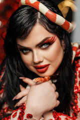 A beautiful young girl plus size model in a red evening dress with bright makeup with a snake. New Year's photo shoot with a snake