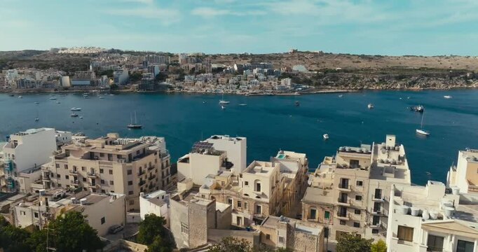 Aerial view of Bugibba on the island of Malta. Urban landscape of the embankment of tourist beaches on the shore of the Mediterranean Sea with a marina with yachts and boats. High quality 4k footage