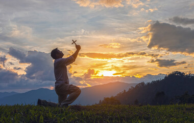 Silhouette Young male kneeling down with holding christian cross for worshipping God on the...