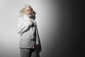 elderly man with white hair in a stylish light suit standing against a gradient background,...