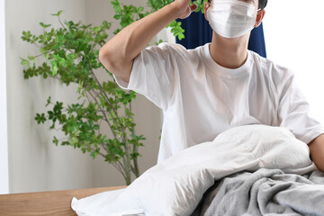 ベッドで頭痛に苦しむマスク姿の若い男性