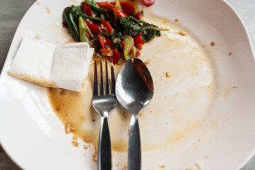 Spoon, forks, tissue paper, and leftover food on the white plastic plate after eating