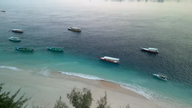 Aerial view of beautiful sandy beach and clear blue ocean with boats, Gilli Trawangan, Indonesia.
