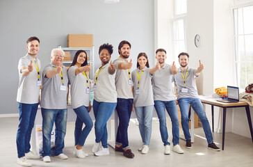 Multiethnic team of happy volunteers gives thumbs up at a humanitarian aid center. People smiles...