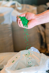 Hand on large pile of blue plastic granules in temporary storage of production line at recycle...