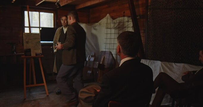 World War 2 era concept - a group of resistance fighters receive a mission briefing from a secret agent in a abandoned hideout. The group leader walks stands up and walks forward