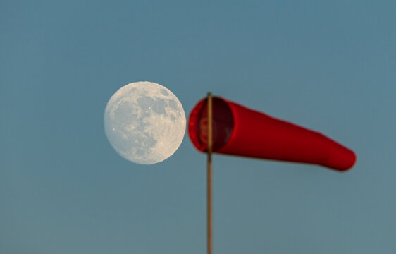 The moon and windsock against a clear blue sky at dusk