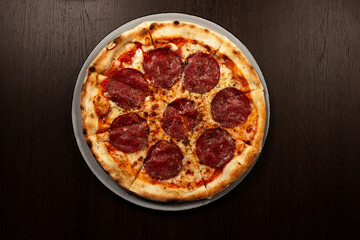 Pizza Salami auf einem Teller auf einem Tisch mit dunklem Holz