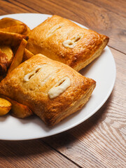 Fototapeta premium Two crispy salmon fish pies and golden wedges on a plate, Close up. Cooked dinner serving. Pastry type product.