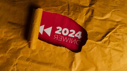 A piece of crumpled brown paper with a small tear in it. Through the tear, a red background is visible with the text "2024 Rewind" written on it. Rewinding time, nostalgia, and looking back concept