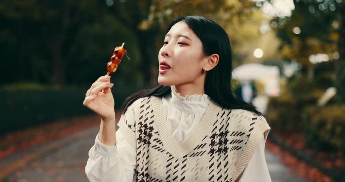 Street food, eating and happy with Japanese woman in park for dessert, traditional cuisine and holiday. Dango, taste and festival season with asian person and culture snack for sweets and lunch