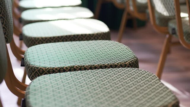Green upholstered theater chairs with intricate diamond patterns in row. Chairs feature wooden frames highlighting detailed fabric design