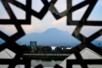 A breathtaking view of Mount Manglayang, an inactive volcano in West Java, Indonesia, framed by an intricate Islamic window design.