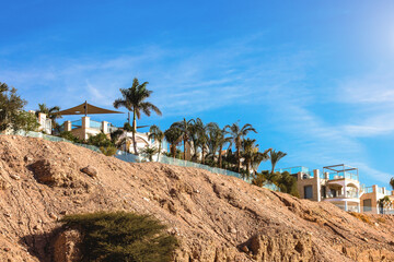 desert village outskirts villa buildings resort apartments settlement sand stone dry nature country side landscape view with palm trees and blue sky background