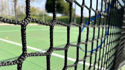 tennis net close-up, blue racket and green court in the background