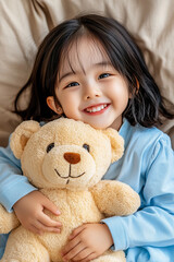 Happy Asian girl with short hair wearing a blue shirt, holding a beloved plush teddy bear, smiling indoors.