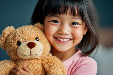 Cheerful young Asian girl with short hair in a shirt, holding her favorite teddy bear, beaming with joy at home.