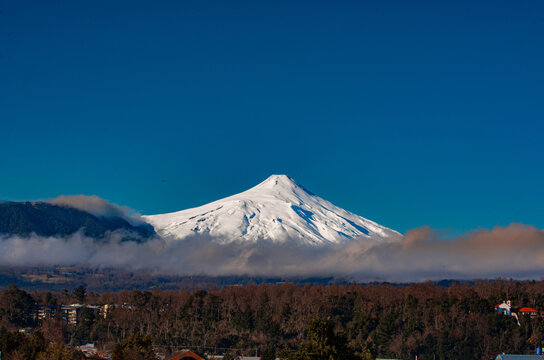 A dramatic moment capturing Villarrica Volcano in eruption, with ash plume rising above the trees in Pucon, Chile.