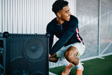 Smiling young man in sportswear turning on a large wireless speaker to play some music before a gym workout session