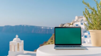 Fototapeta premium Laptop with green screen on a table overlooking Santorini's famous white and blue architecture, sunlit Aegean Sea in the background 