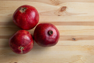 A whole pomegranates on a rustic wooden surface. Three fresh ripe pomegranates. A healthy fruit with lots of vitamins. Natural image.