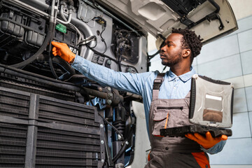 Experienced mechanic standing by the truck with hood opened checking the engine and cooling system.