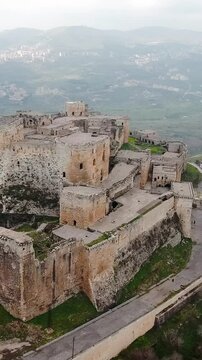 Aerial view of well-preserved Crusader castle Krak of Chevaliers on cloudy day, vertical video.