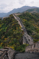 Great Wall of China, extreme path with bricks wall and vertical steps between the watchtowers, surrounded by dramatic landscape of mountains and forest in autumn; near Beijing, China