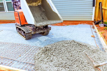 Heavy machinery dispenses fresh concrete onto prepared area for new patio workers guide process in...