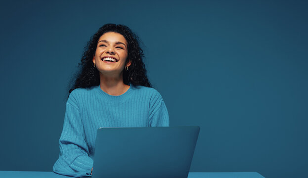 Happy female student thinking and studying at desk with laptop in monochromatic setting