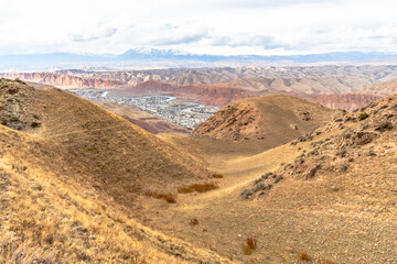 A serene valley with golden hills leading down to a small town nestled among red rock formations. A...