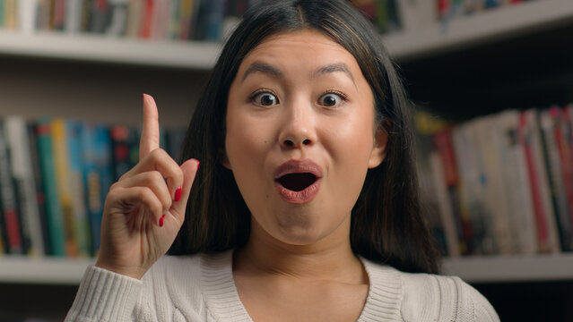 Female portrait smiling happy asian woman girl student 20s looking at camera in university library showing thumbs up like gesture approval symbol successful feedback recommendation agree great result