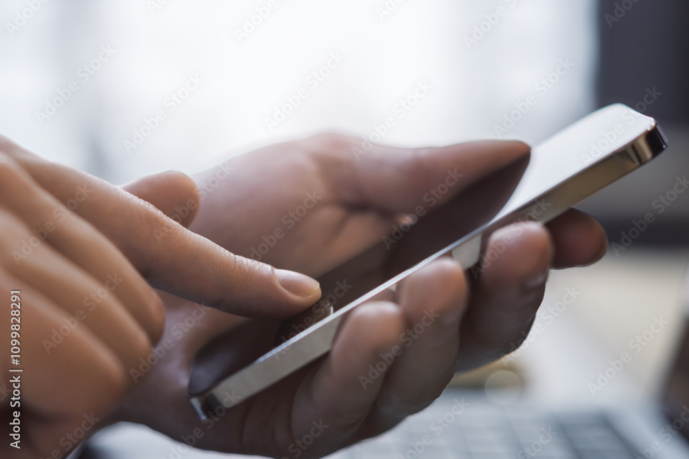 Poster man deeply focused on his modern smartphone, laptop in the background within a softly blurred office