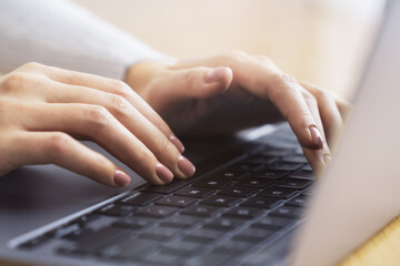 A woman's hands are seen in close-up, typing on a contemporary laptop keyboard, office surroundings...