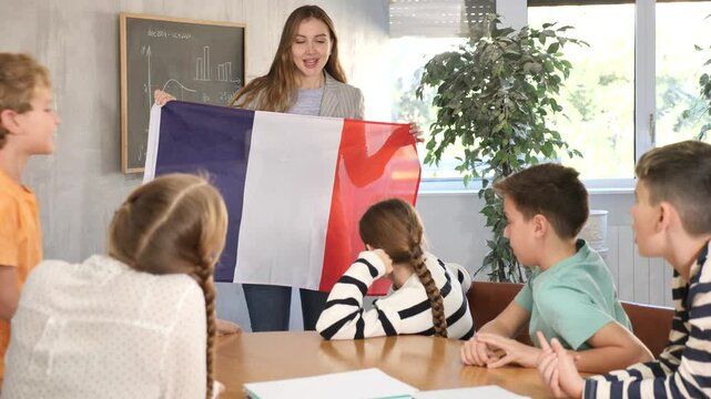 Decent teacher showing France flag to group of preteen schoolchildren in classroom during lesson . High quality 4k footage