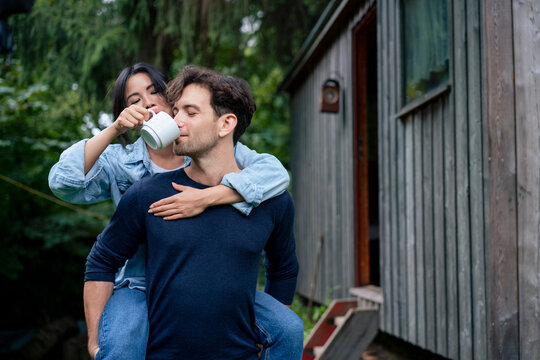 Woman with man drinking coffee through cup near log cabin