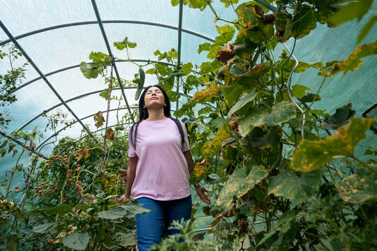 Woman with eyes closed walking near plants in greenhouse