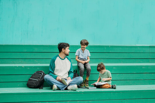 Father sitting with boys on green steps near wall