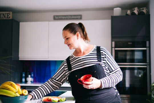 Smiling woman holding coffee cup and arranging kitchen at home