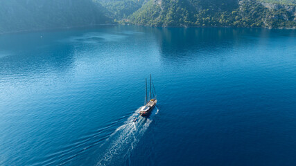 A gulet ship anchored near turquoise waters, with green hills in the background, creating a serene...