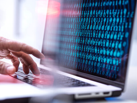 Hacker working over binary codes on laptop