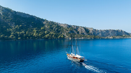 A gulet ship anchored near turquoise waters, with green hills in the background, creating a serene and picturesque scene. © ALPSARAL