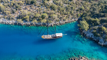 A gulet ship anchored in crystal-clear waters, surrounded by lush green hills and a serene coastal landscape. © ALPSARAL