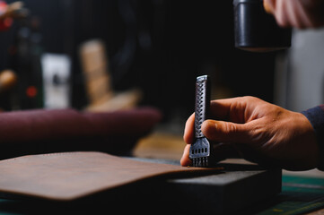 Production process. Young focused experienced master craftsman makes leather goods at his workplace