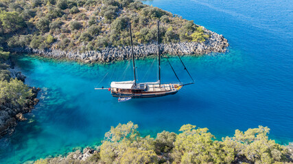 A gulet ship anchored in crystal-clear waters, surrounded by lush green hills and a serene coastal landscape. © ALPSARAL