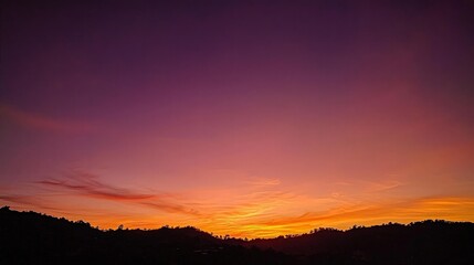Obraz premium Vibrant sunset over silhouetted hills.